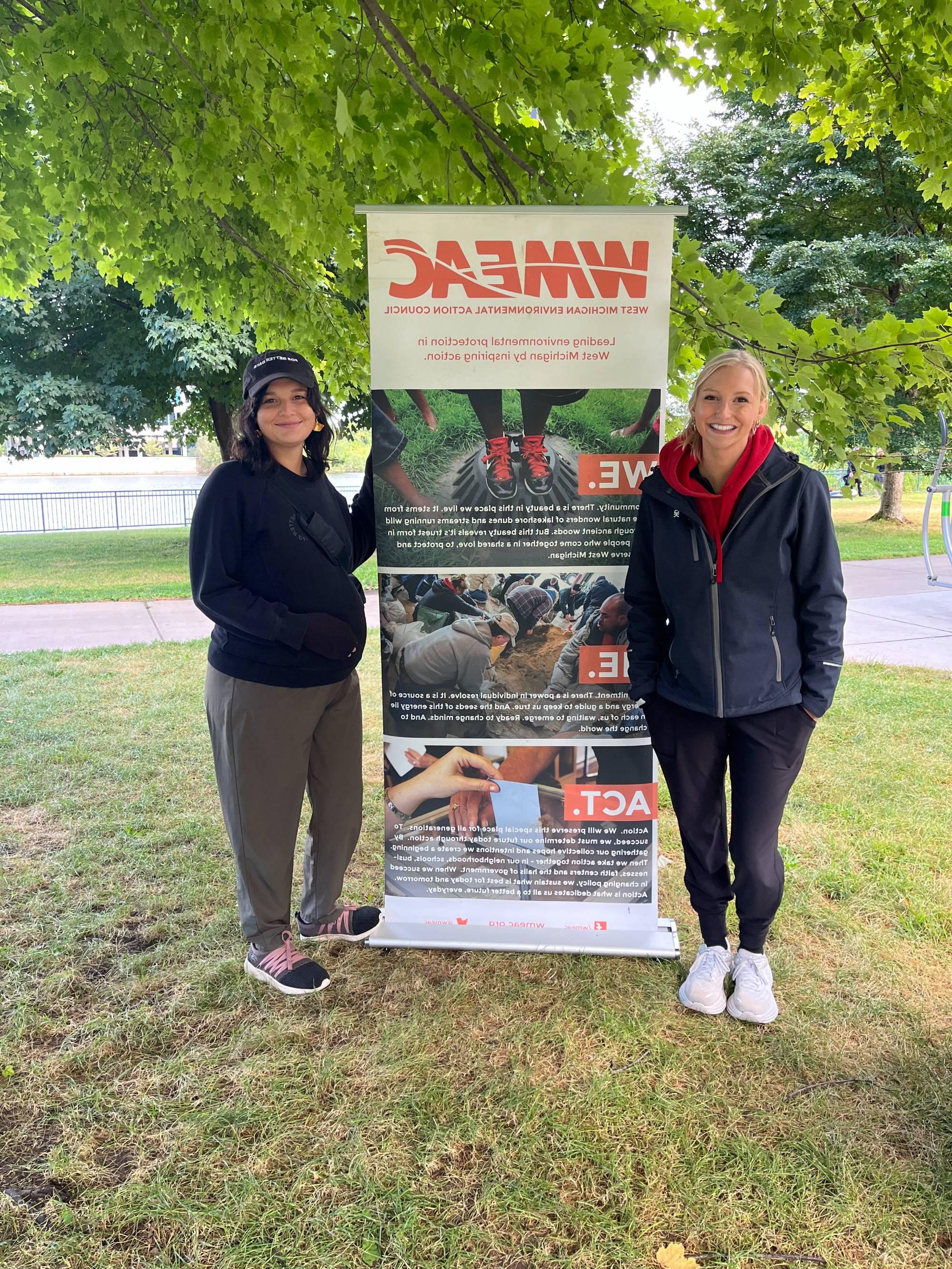 Two GLISA Team members standing in front of a banner at the Grand River Clean Up.